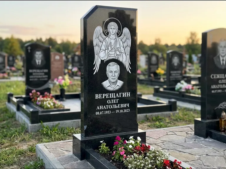 Памятник с гравировкой иконы: стела с резным навершием и нимбом в золоте — гравировка образа Спасителя, высокие разросшиеся туи полукругом, работа «Мельникова» в Волгограде