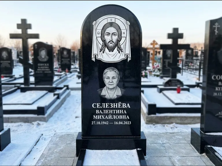 Памятник с гравировкой иконы: небольшая скромная одиночная стела с именной иконой — золочёный нимб на образе, аккуратный участок с газоном, работа «Ковалёв» в Волгограде