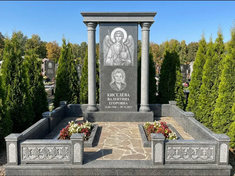 Памятник с гравировкой иконы: массивная стела с двускатным навершием-домиком — гравировка Николая Чудотворца, живая изгородь из туи, работа «Журавлёв» в Волгограде