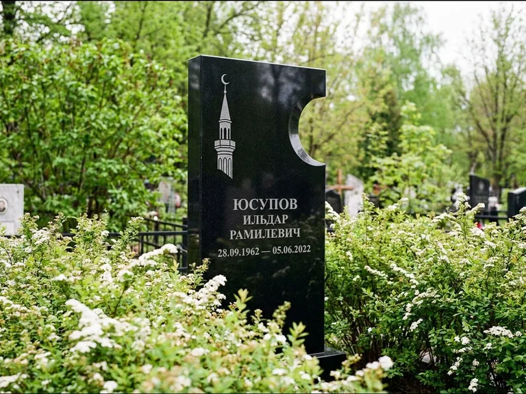 Мусульманский памятник с гравировкой мечети: стела с боковым вырезом в форме полумесяца — гравировка минарета с полумесяцем, низкие кусты спиреи в цвету, работа «Юсупов» в Волгограде
